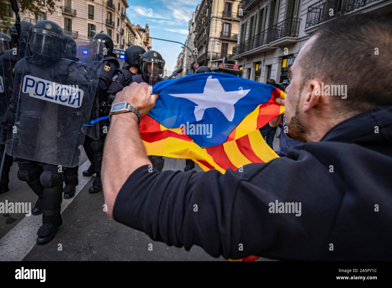 Un dimostrante detiene un'indipendenza bandiera alla catalana ufficiali della polizia durante la manifestazione.il sesto giorno di protesta dopo l'annuncio delle sentenze da parte della Corte suprema di Spagna che condanna il catalano e i leader politici a lunghe pene detentive. Il agenti antisommossa hanno ripetutamente caricato i manifestanti intorno della stazione centrale di polizia della polizia nazionale in Via Laietana. Foto Stock