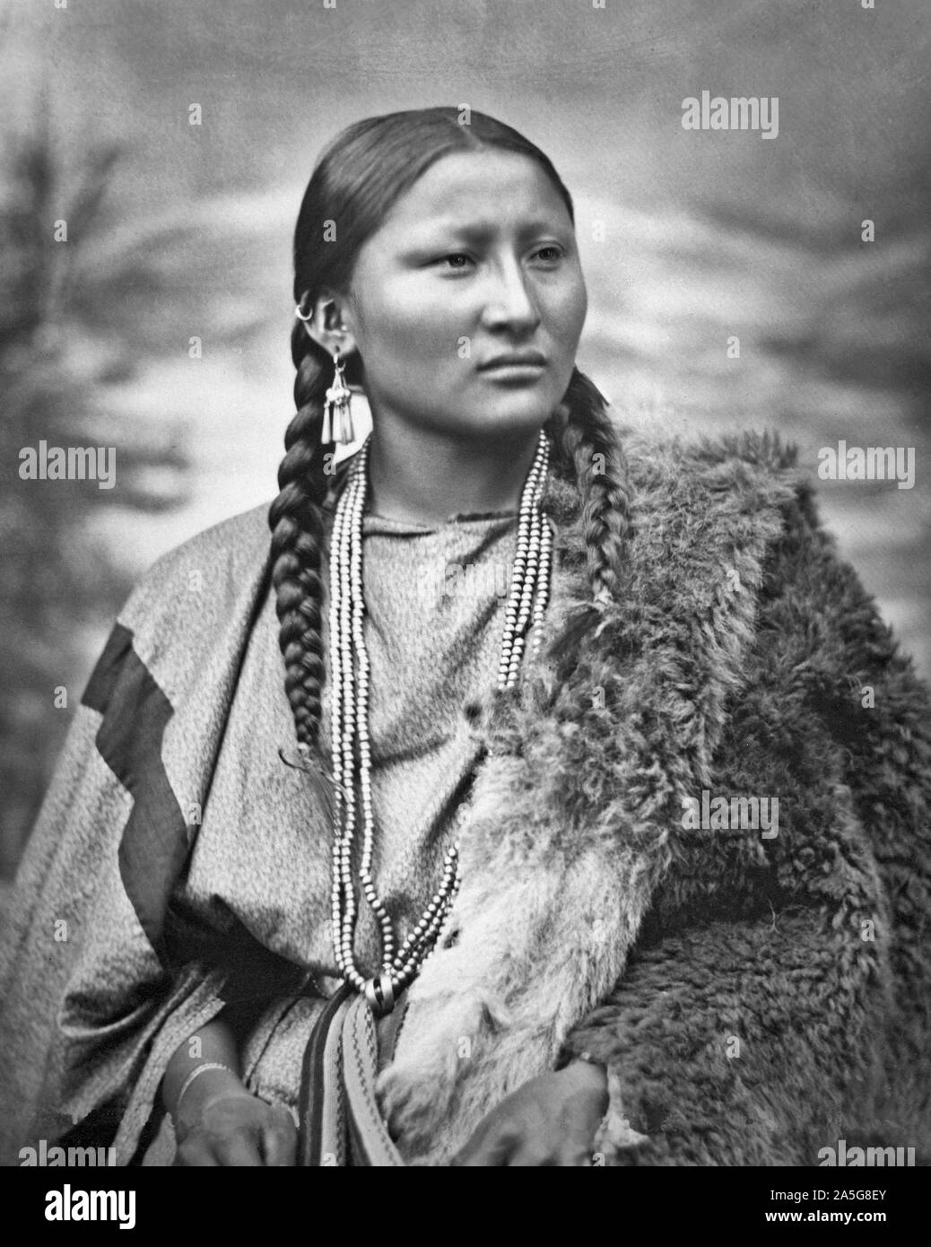 Cheyenne o Arapaho donna graziosa naso a Fort Keogh, Montana, Stati Uniti. Indossa abiti di stoffa con tessuto della cinghia e buffalo robe, così come orecchini, bracciali, anelli e collana. Collotipia. 1879 Foto Stock