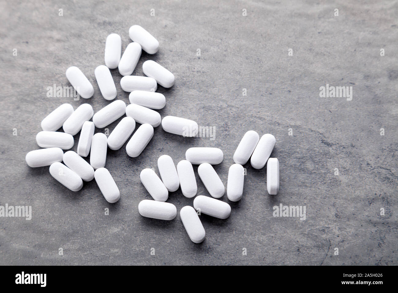 Closeup sparsi medicina bianco vitamine, pillole, farmaci su sfondo grigio. Alimento bianco integratore dietetico. La fotografia in bianco e nero. Vista superiore Foto Stock