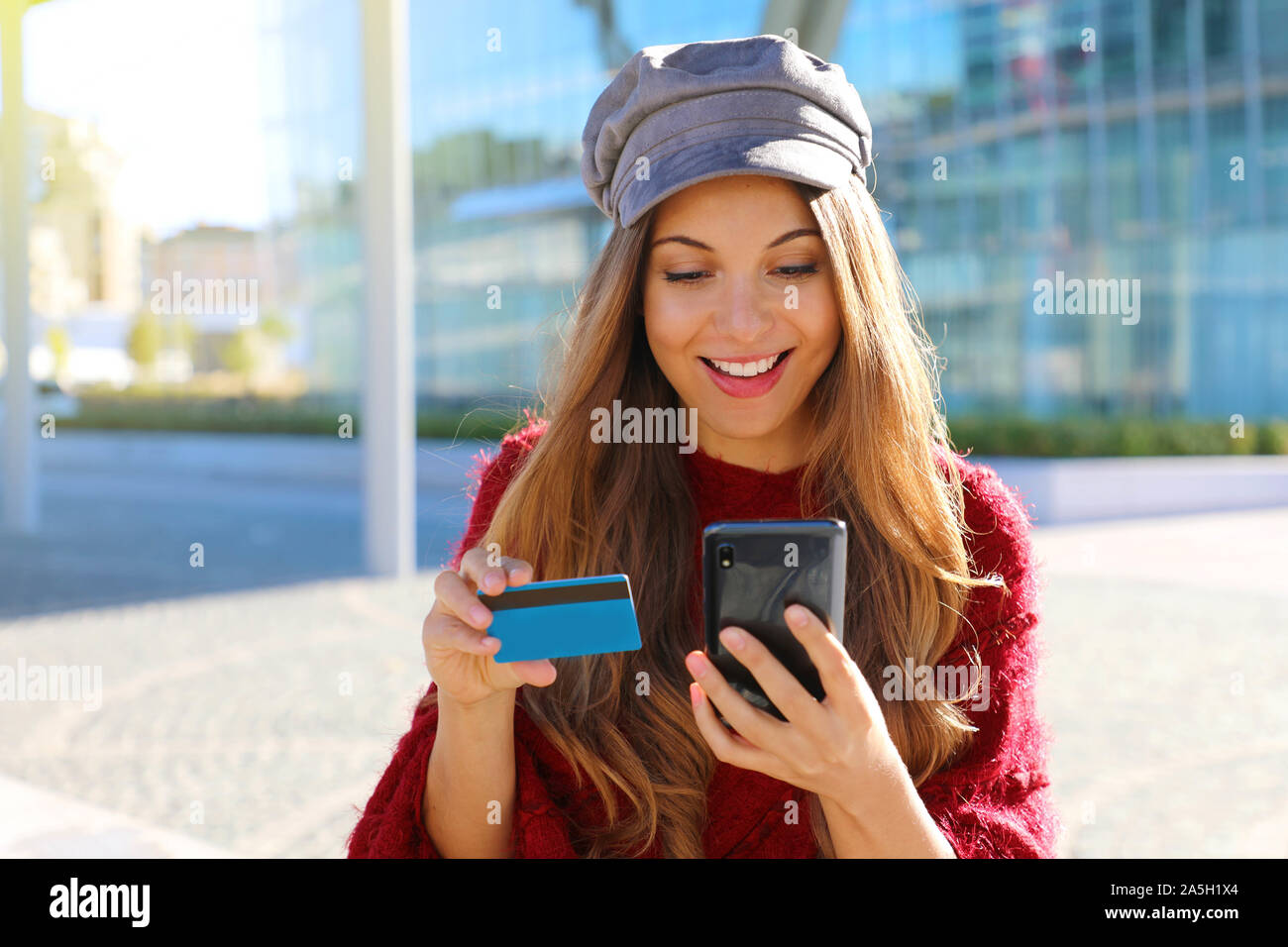 Bella donna moda inserire il numero di carta di credito acquisto online con smart phone seduti all'aperto. Foto Stock