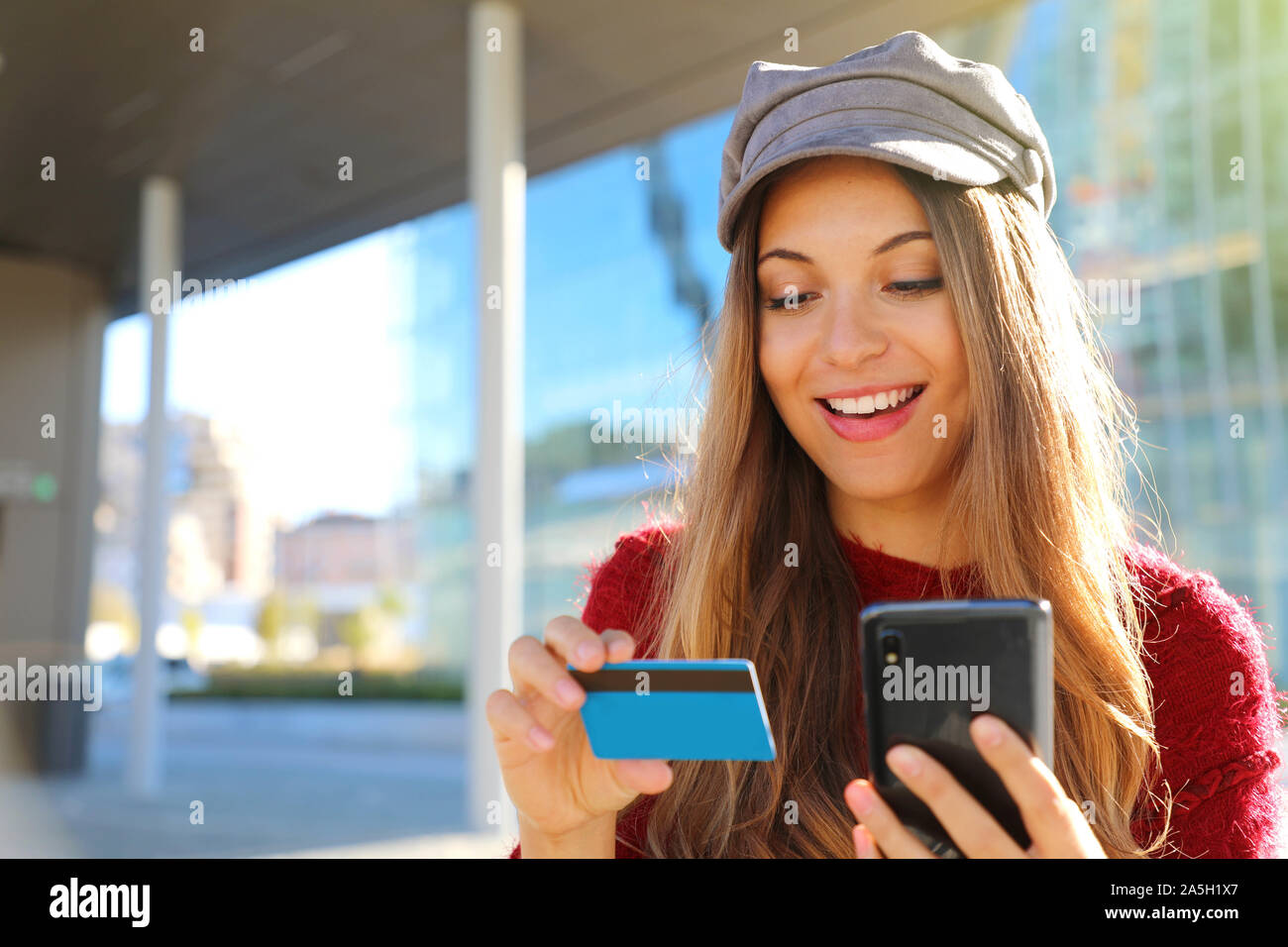 Moda Donna leggendo il numero di carta di credito acquisto online con smart phone seduti all'aperto. Foto Stock