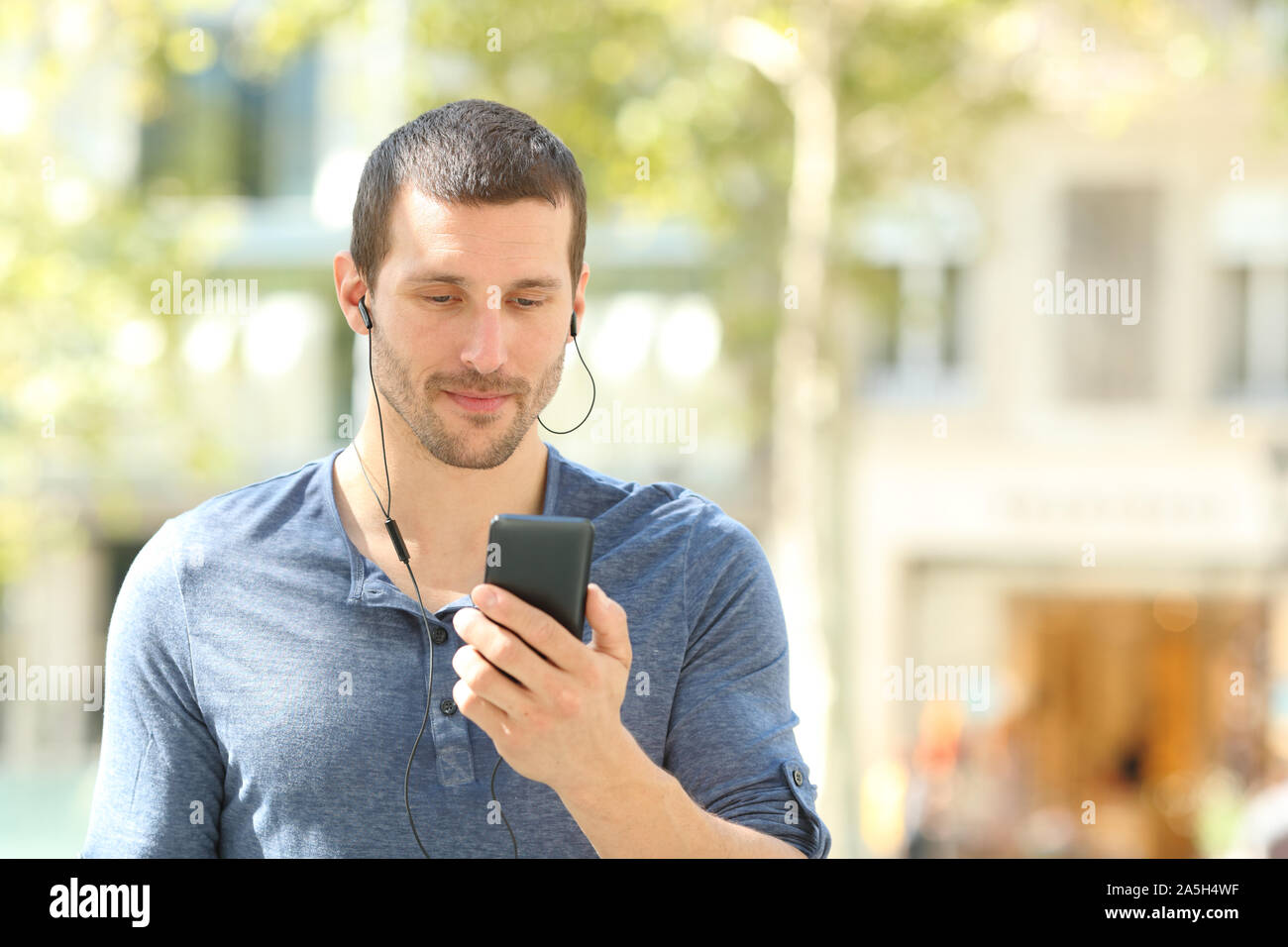 Vista frontale di un uomo adulto ascoltare musica controllo telefono cellulare a piedi in strada Foto Stock