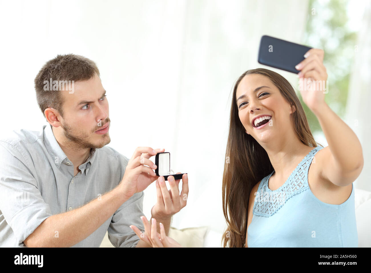 Turbare l uomo una proposta di matrimonio e la ragazza tenendo selfie seduto su un divano a casa Foto Stock