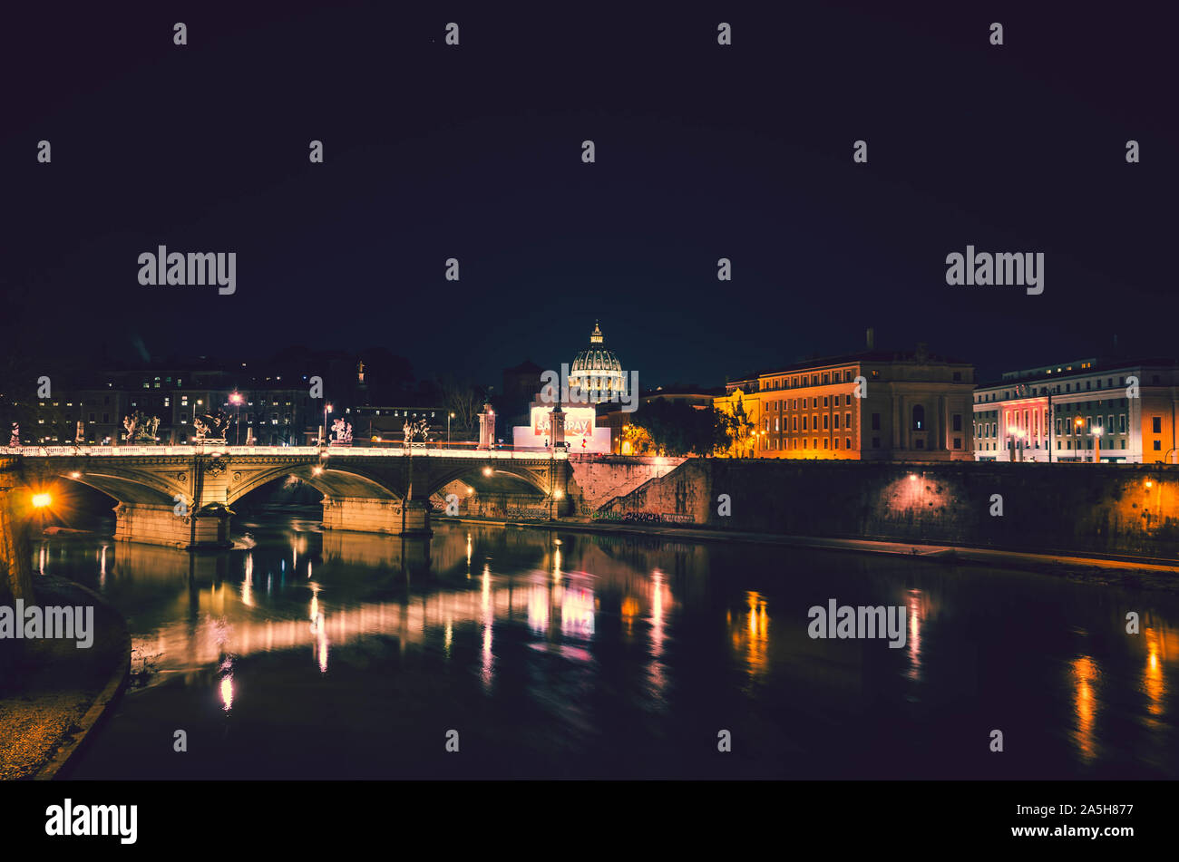 Vista notturna di Roma.In primo piano il fiume Tevere e il suo incredibile ponti e sullo sfondo la cupola della basilica di San Pietro. Foto Stock