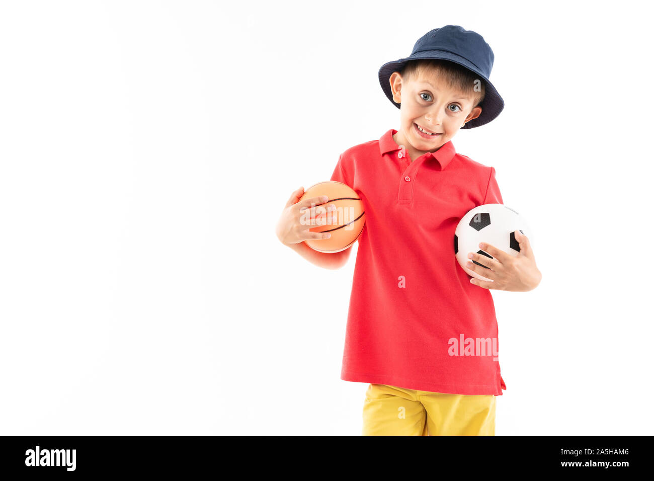 Un ragazzino in panama, maglia gialla, pantaloncini rosso e bianco sneakers  stand con campi da basket e palloni da calcio Foto stock - Alamy