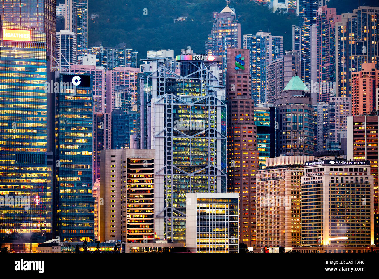 Edifici alti e moderni sul fronte acqua centrale illuminati di notte. Hong Kong, Cina. Foto Stock