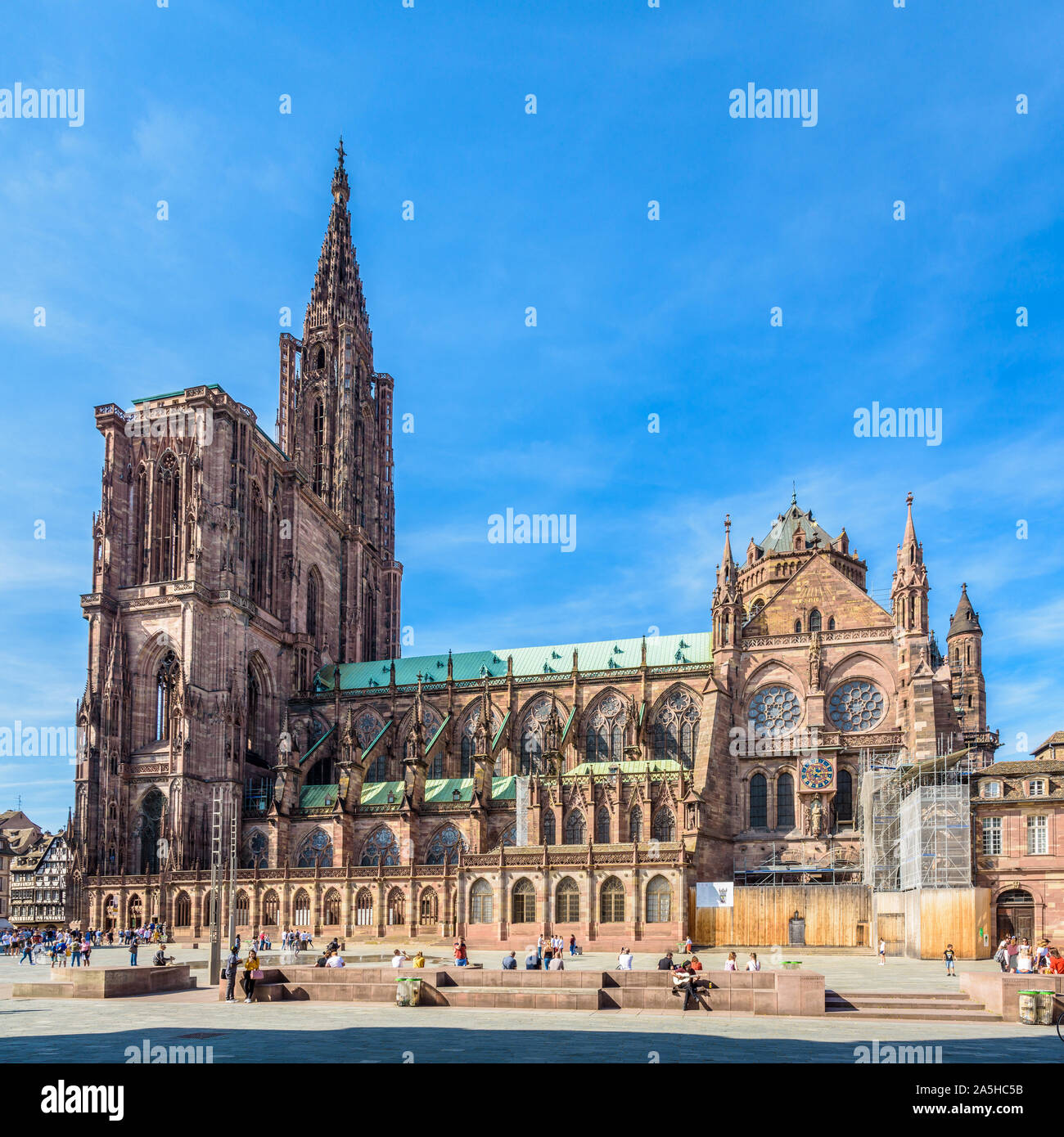 La guglia e il lato meridionale della cattedrale di Notre Dame a Strasburgo, in Francia, in una giornata di sole con persone che passeggiano e rilassante sulla place du Chateau. Foto Stock