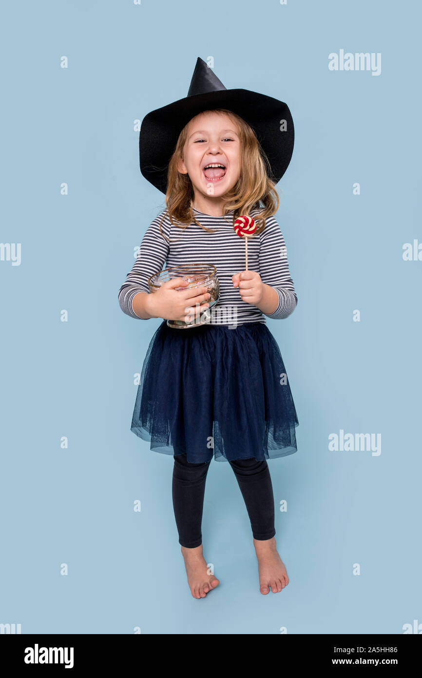 Ritratto di una ragazzina in witch hat holding lecca-lecca e vaso pieno di chicche Foto Stock