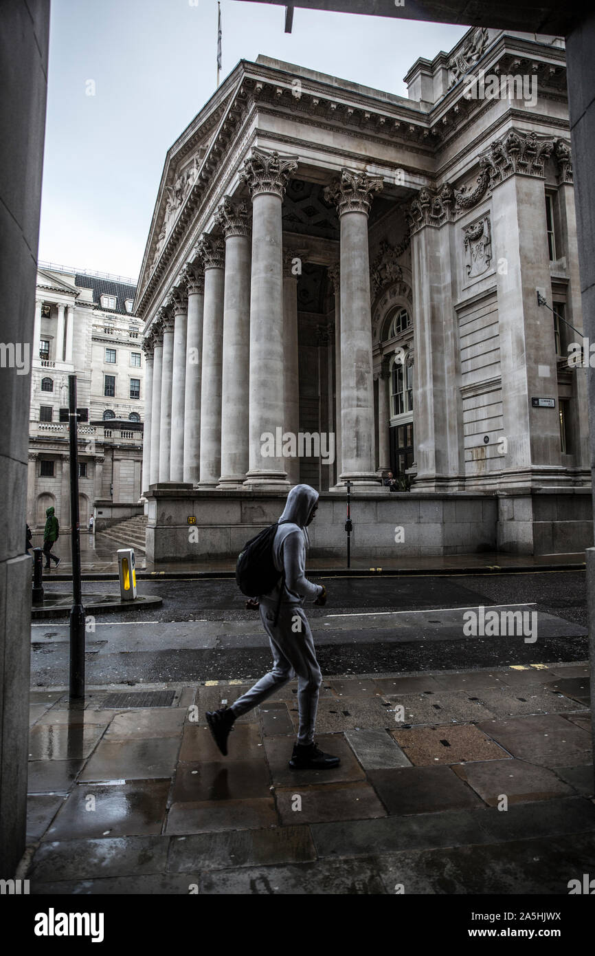 Un uomo incappucciato passeggiate passato il Royal Exchange nella City di Londra il quartiere delle banche e della finanza in un pomeriggio autunnale, London, England, Regno Unito Foto Stock