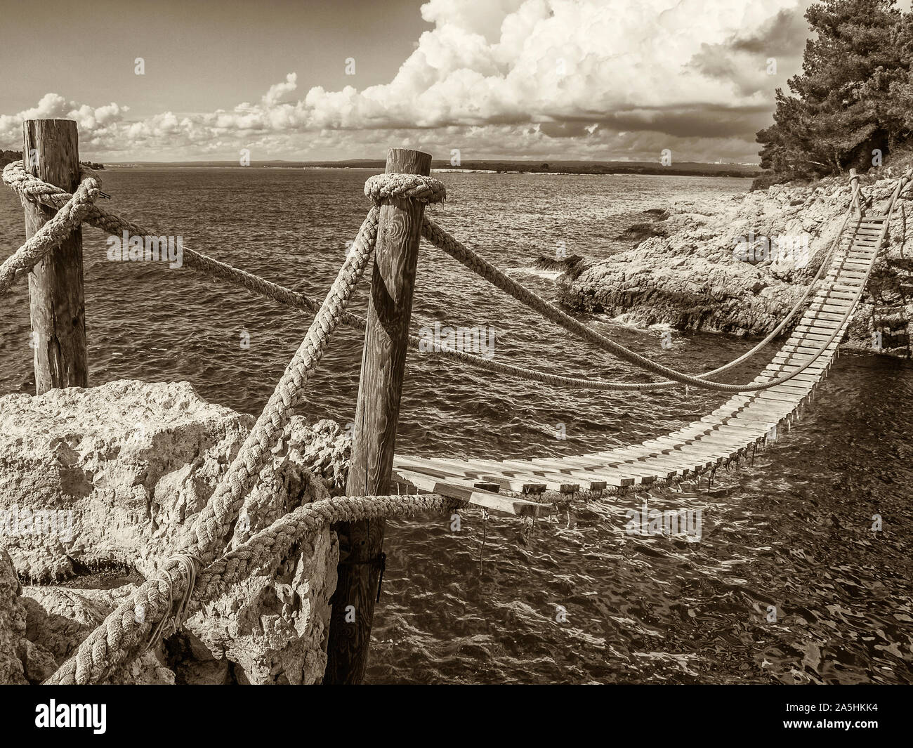 Appendere il ponte di legno collegare rocciosa costa del mare, tonalità seppia Foto Stock