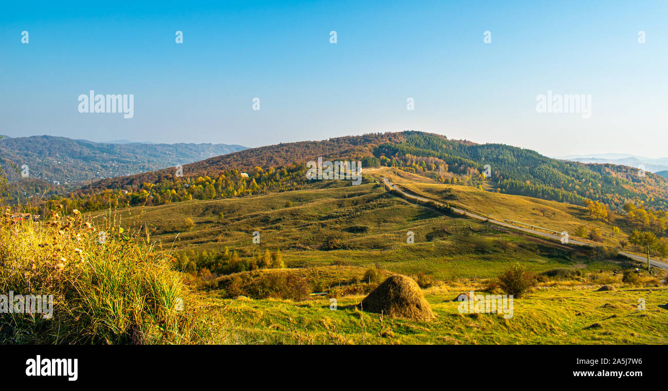 Serata sole su di una bellissima collina nei pressi di un piccolo villaggio, con pochi alberi e i colori autunnali Foto Stock