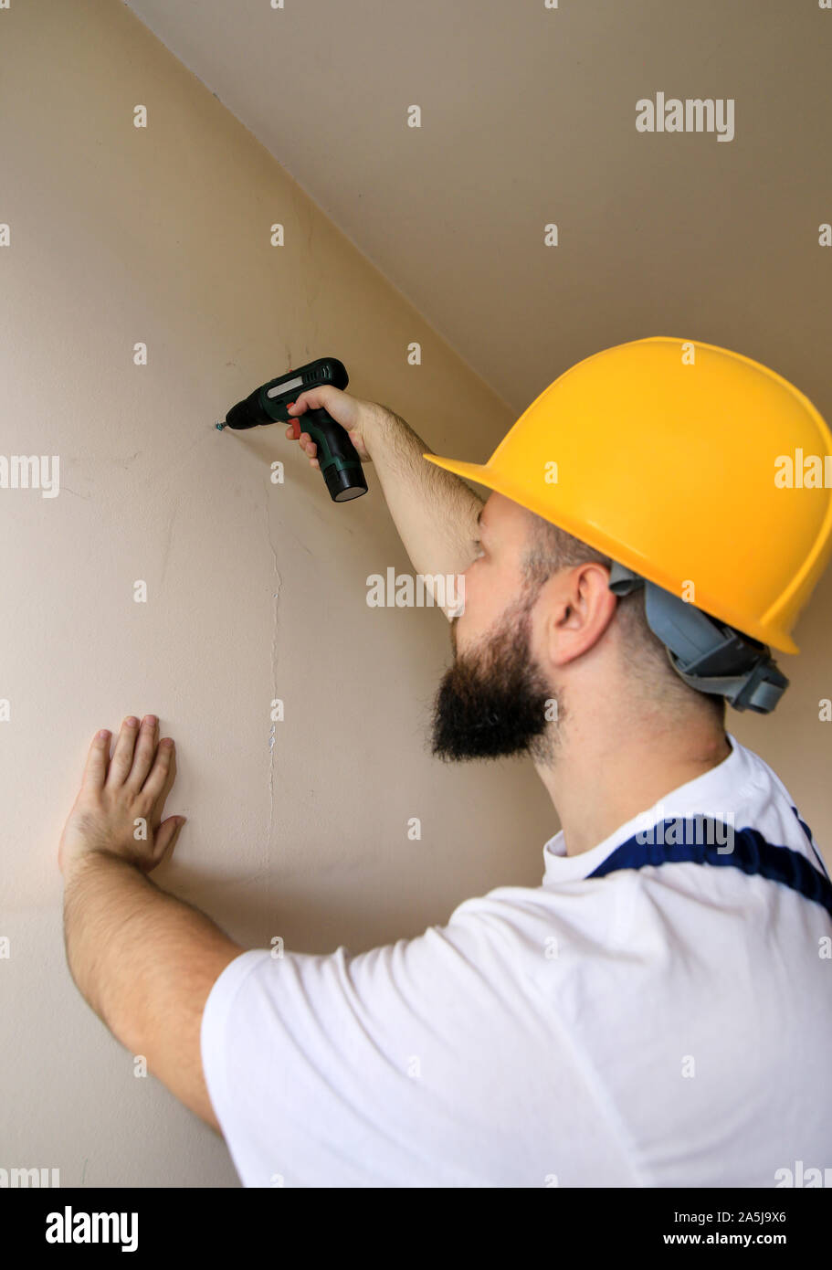 Lavoratore edile e tuttofare lavora sulla ristrutturazione di appartamento. Builder mediante cacciavite elettrico e avvitando la vite al di fuori del muro. Foto Stock