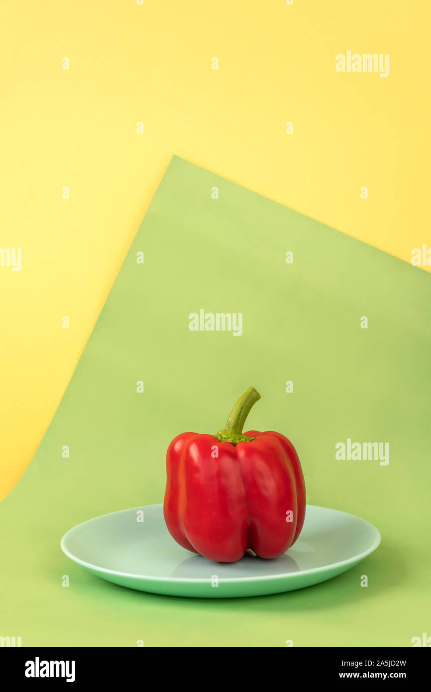 Composizione minimalista di peperone rosso, blu giallo piastra di sfondo verde Foto Stock