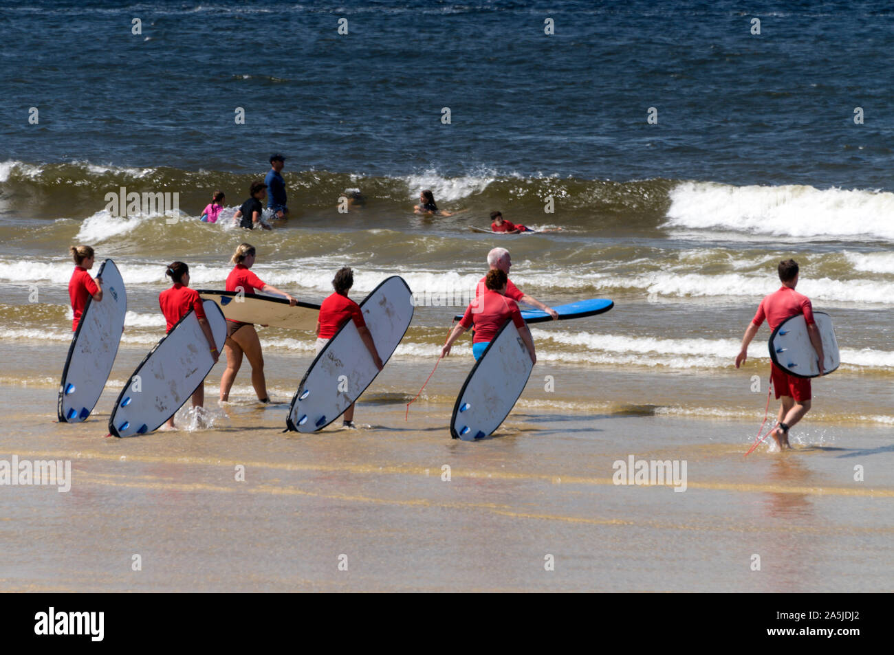 Un gruppo di giovani che trasportano le loro tavole da surf al mare per una tavola da surf lezione a teste di Noosa sulla Sunshine Coast in Queensland, Australia Foto Stock
