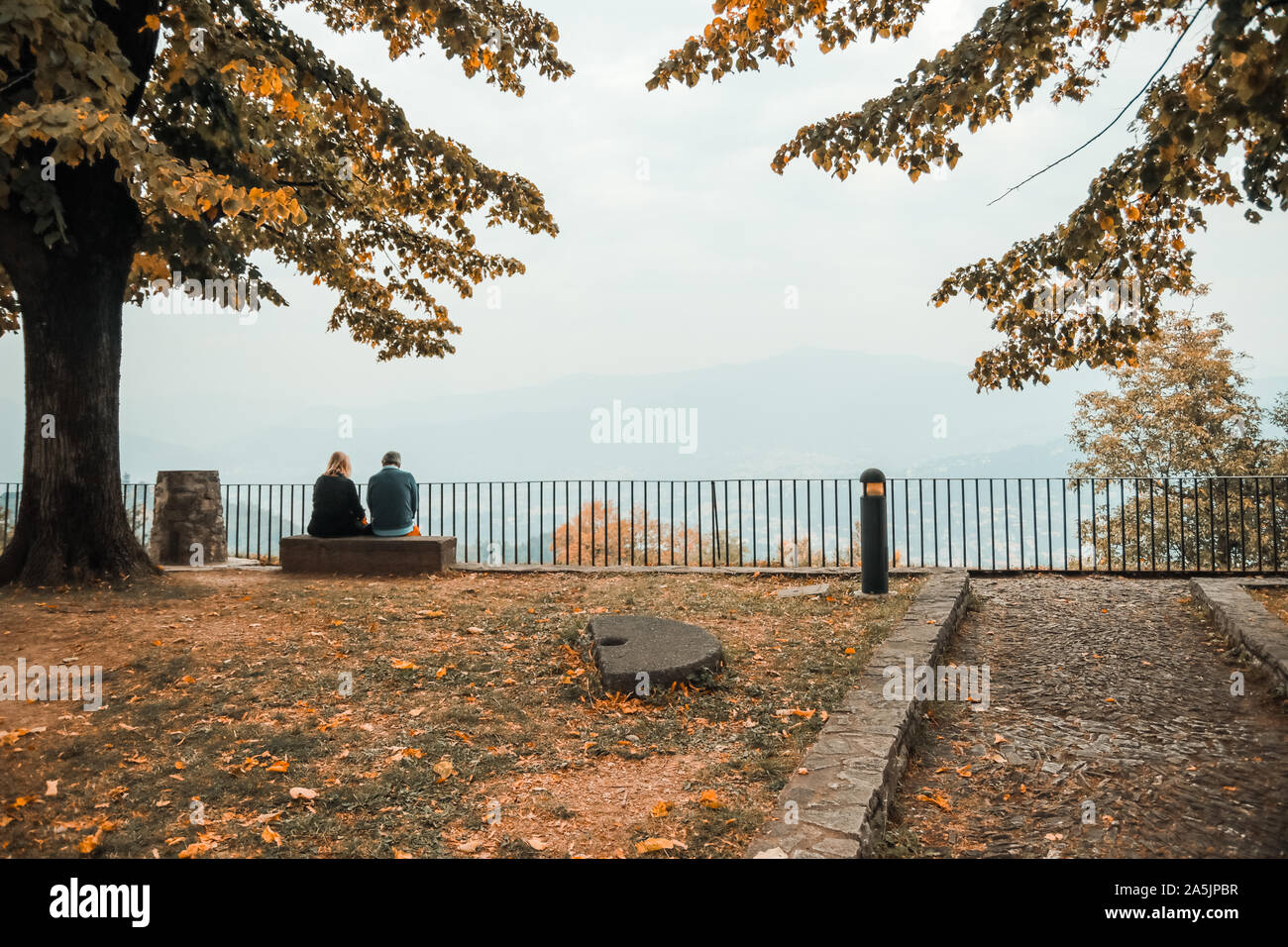 Adulto Giovane seduto su una panchina nel parco che circonda gli alberi e nella parte anteriore di una bella vista sulla montagna. Le nuvole, l'autunno. Foto Stock