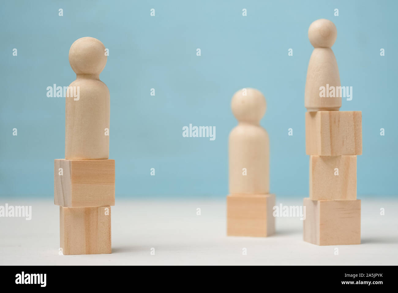 Abstract tre figure in legno di persone stand su diversi livelli sono fatti di blocchi giocattolo su sfondo blu. Foto Stock
