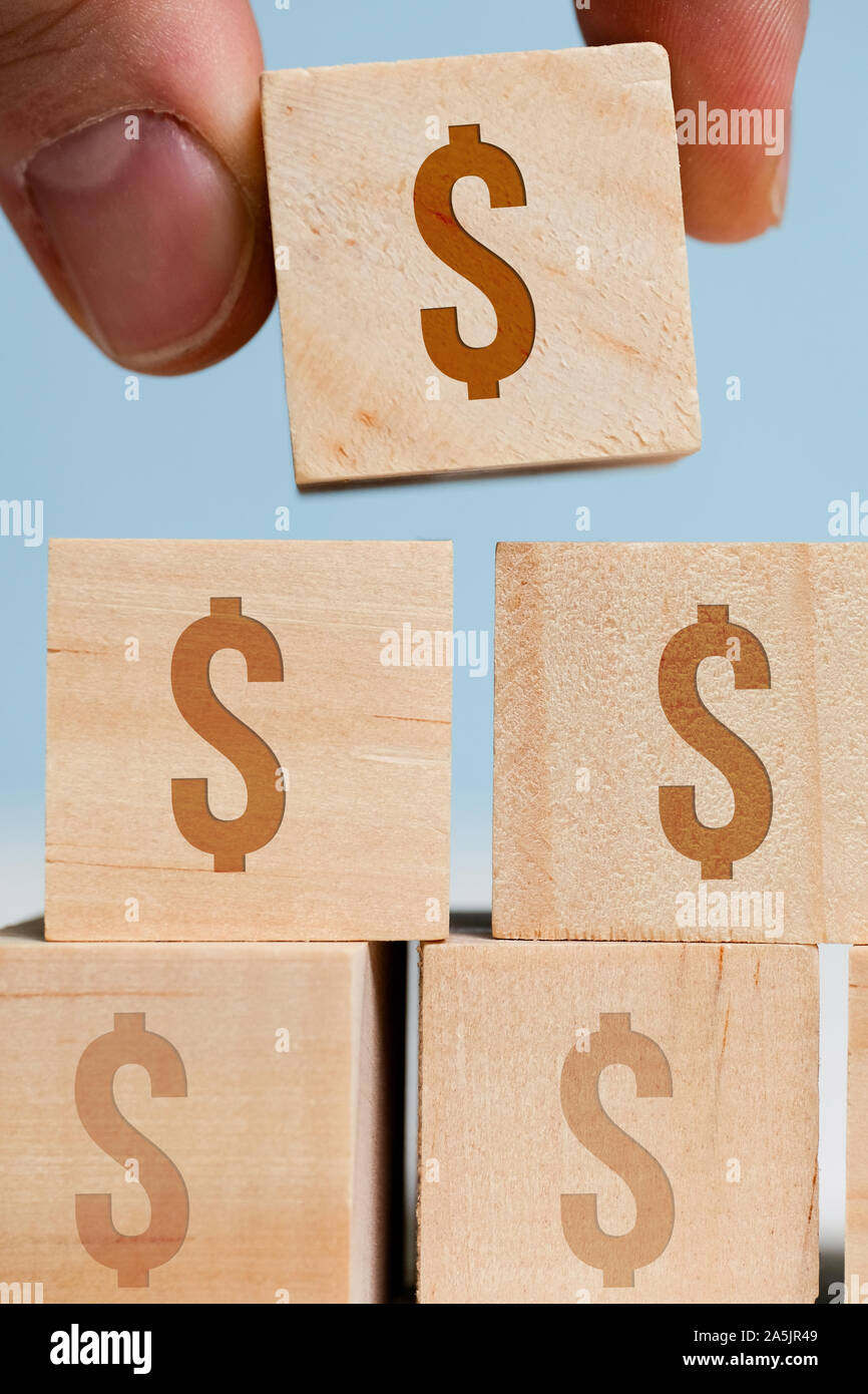 Tenere le dita a cubetti con un US dollar sign su uno sfondo blu. Il concetto di accumulo di denaro, capitali. Close up. Verticale. Foto Stock