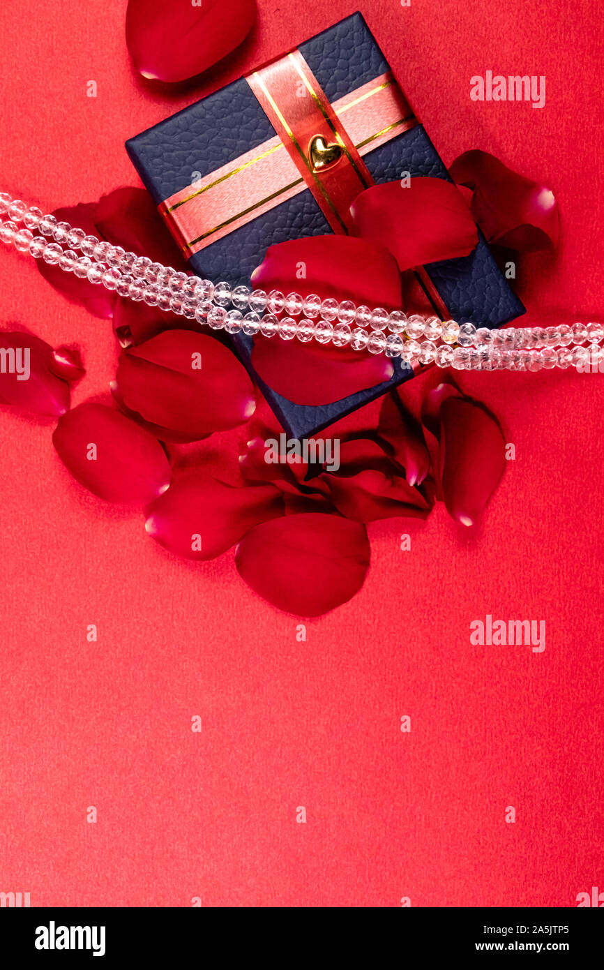 Decorate in blu confezione regalo con petali di rosa e gioielli di cristallo su sfondo rosso con spazio di copia Foto Stock