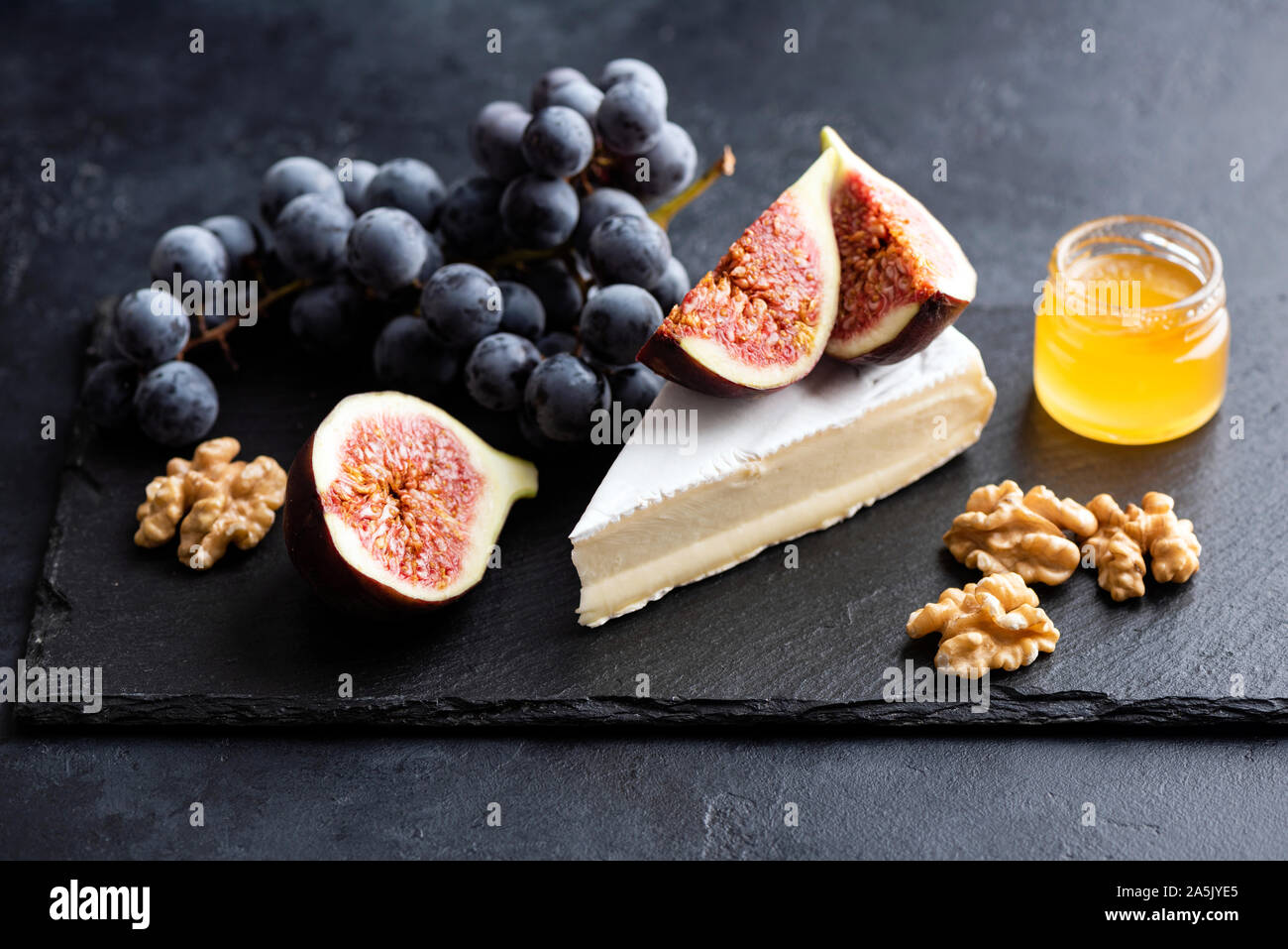 Brie o formaggio camembert board con noci, uva, fichi e miele servite su nero ardesia piastra. Antipasto Gourmet Foto Stock