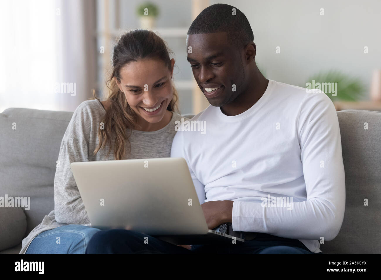 Felice coppia internazionale rilassarsi a casa utilizzando laptop Foto Stock