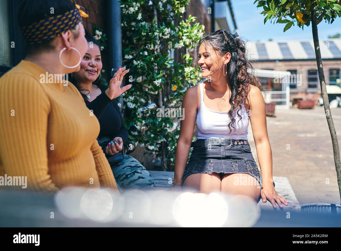 Giovane donna e la sua teenage sorelle seduta sul tavolo esterno in chat Foto Stock