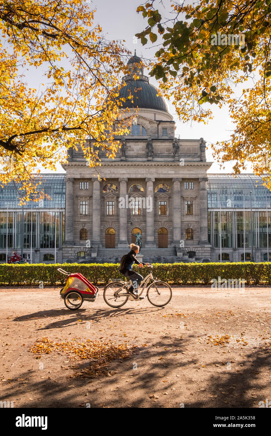 Hofgarten, Monaco di Baviera, Germania. Una giovane donna in bicicletta nel Hofgarten durante l'autunno (ottobre) vicino bavarese della Cancelleria di Stato edificio. Foto Stock