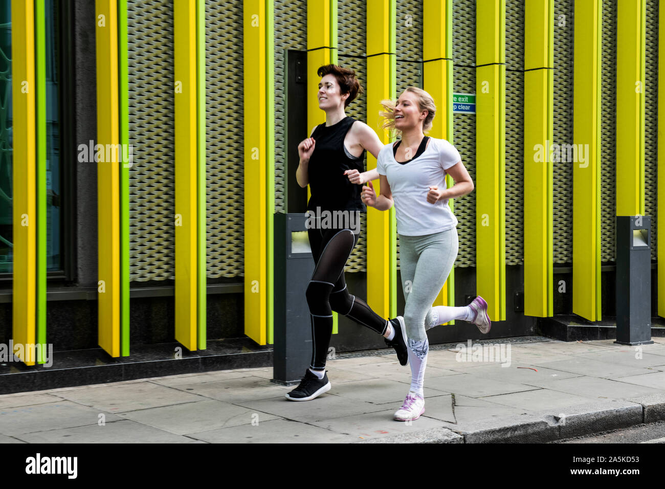 Due giovani donne che corre lungo il marciapiede della città a piena lunghezza Foto Stock