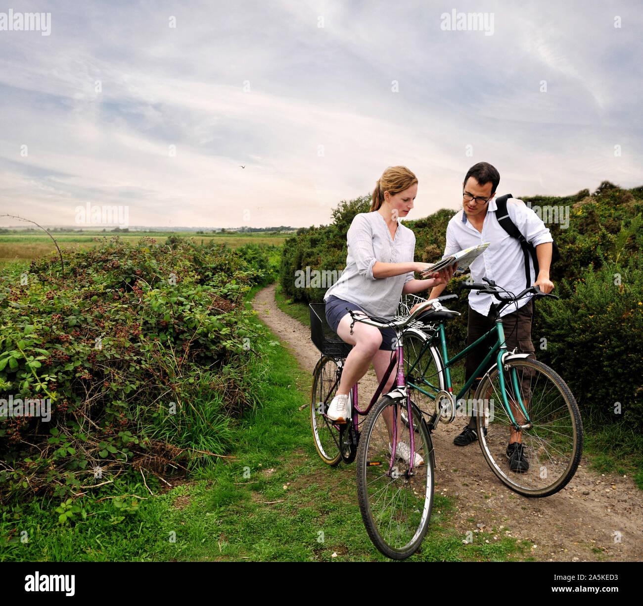La metà degli adulti coppia ciclismo su rurale sterrata guardando la mappa, Southwold, Suffolk, Regno Unito Foto Stock