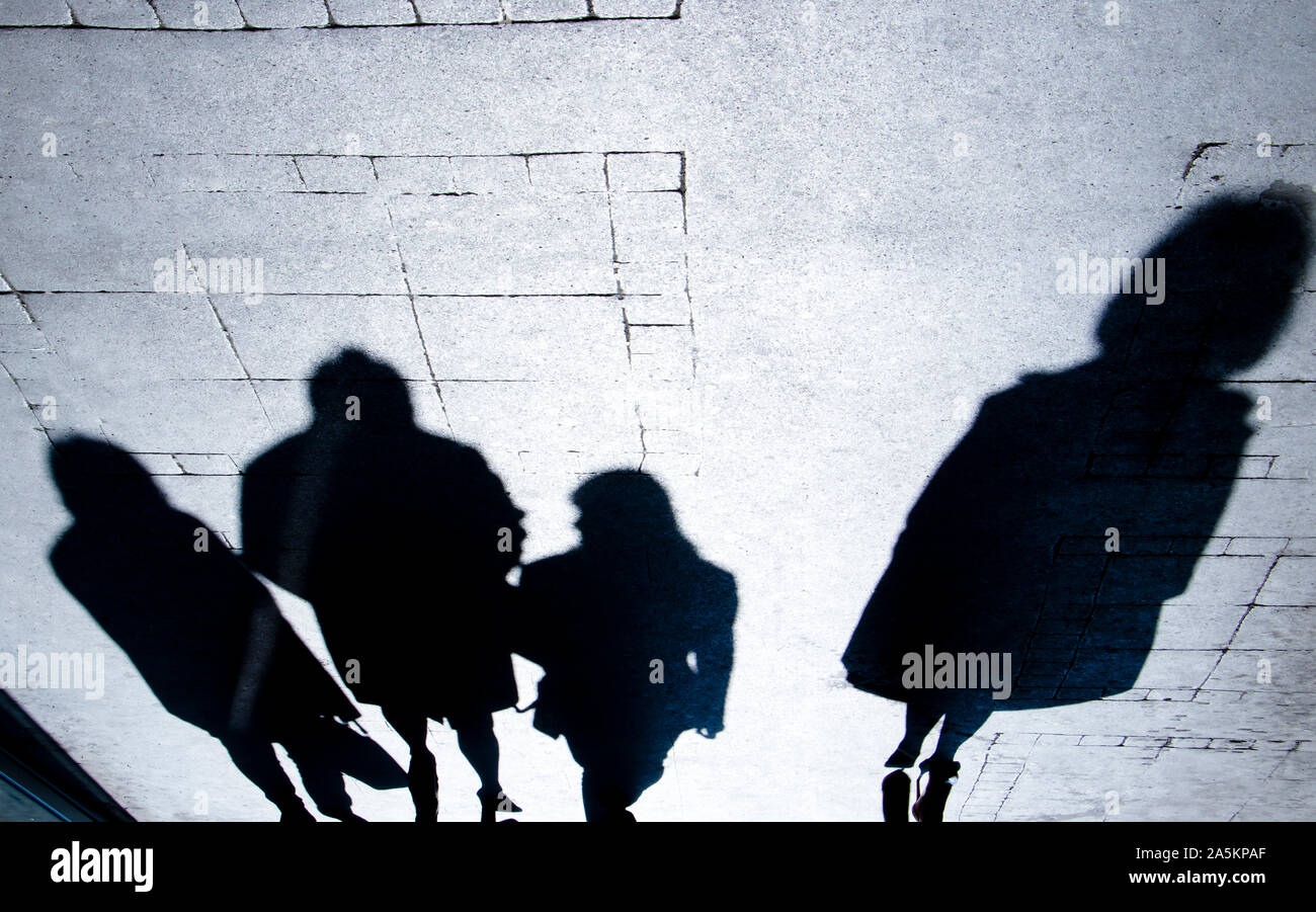 Sfocata ombra silhouette di persone che camminano nella notte e una donna in piedi da solo, su una strada di città marciapiede in alto contrasto bianco e nero Foto Stock