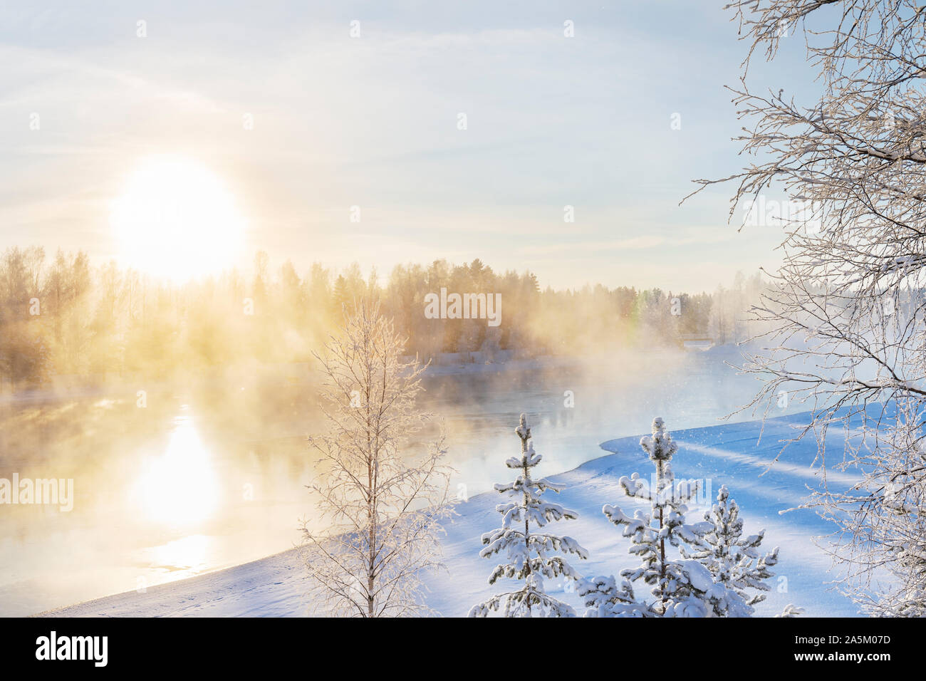 Foschia sopra il fiume di congelamento sulla soleggiata una fredda giornata invernale. Alberi coperti con il gelo e la neve. Foto Stock