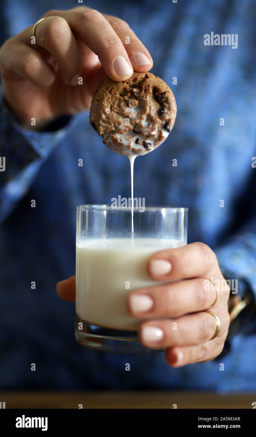 Close up della donna di immersione a mano con pezzetti di cioccolato nel bicchiere di latte Foto Stock