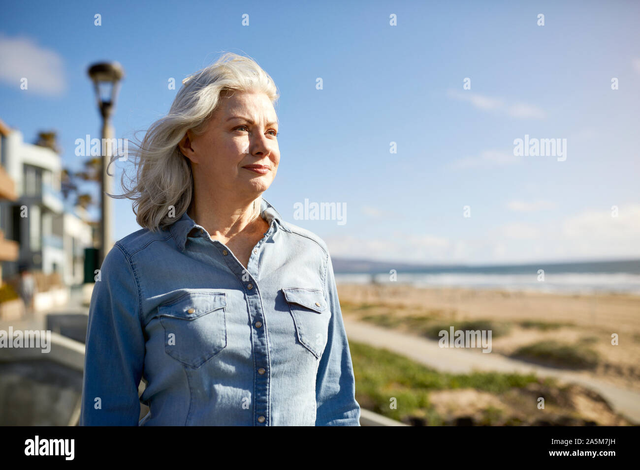 Riflessivo senior woman standing a Manhattan Beach contro sky durante la giornata di sole Foto Stock