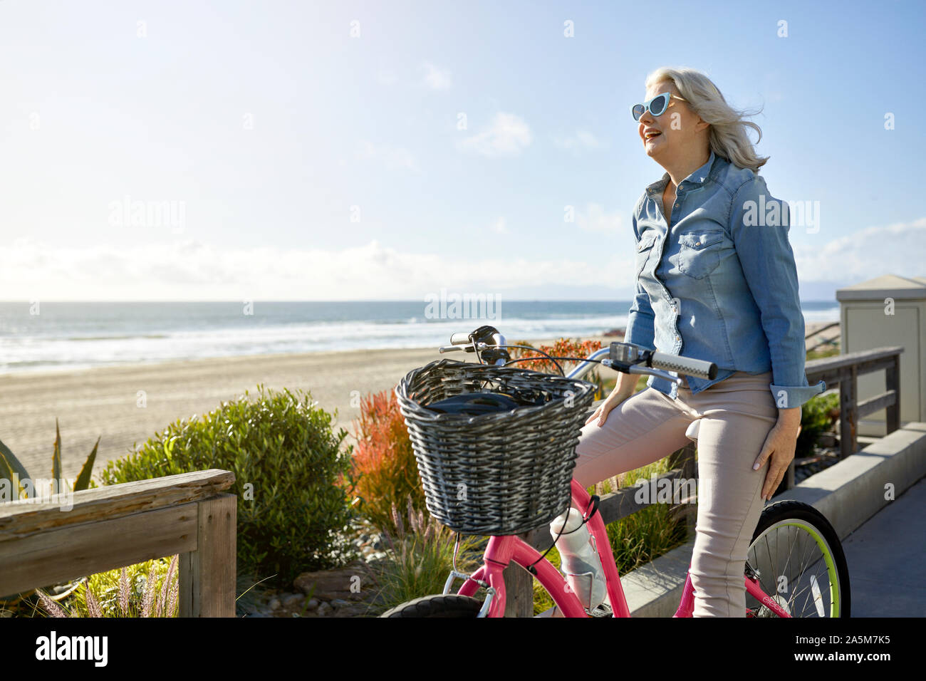 Sorridente donna senior con noleggio biciclette in piedi a Manhattan Beach contro sky durante la giornata di sole Foto Stock