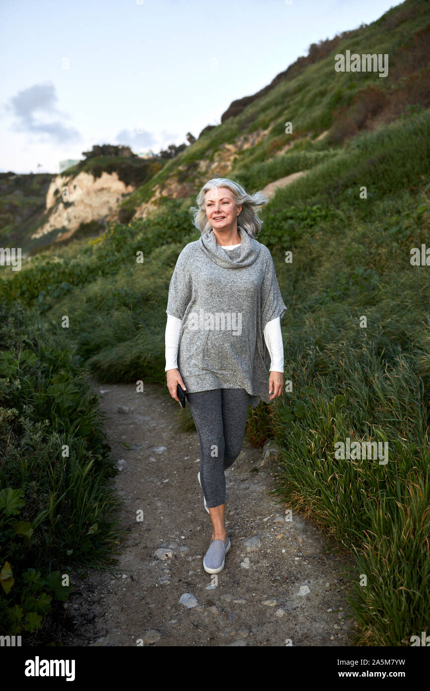 Lunghezza completa di senior Donna che cammina sul sentiero a Manhattan Beach durante il tramonto Foto Stock