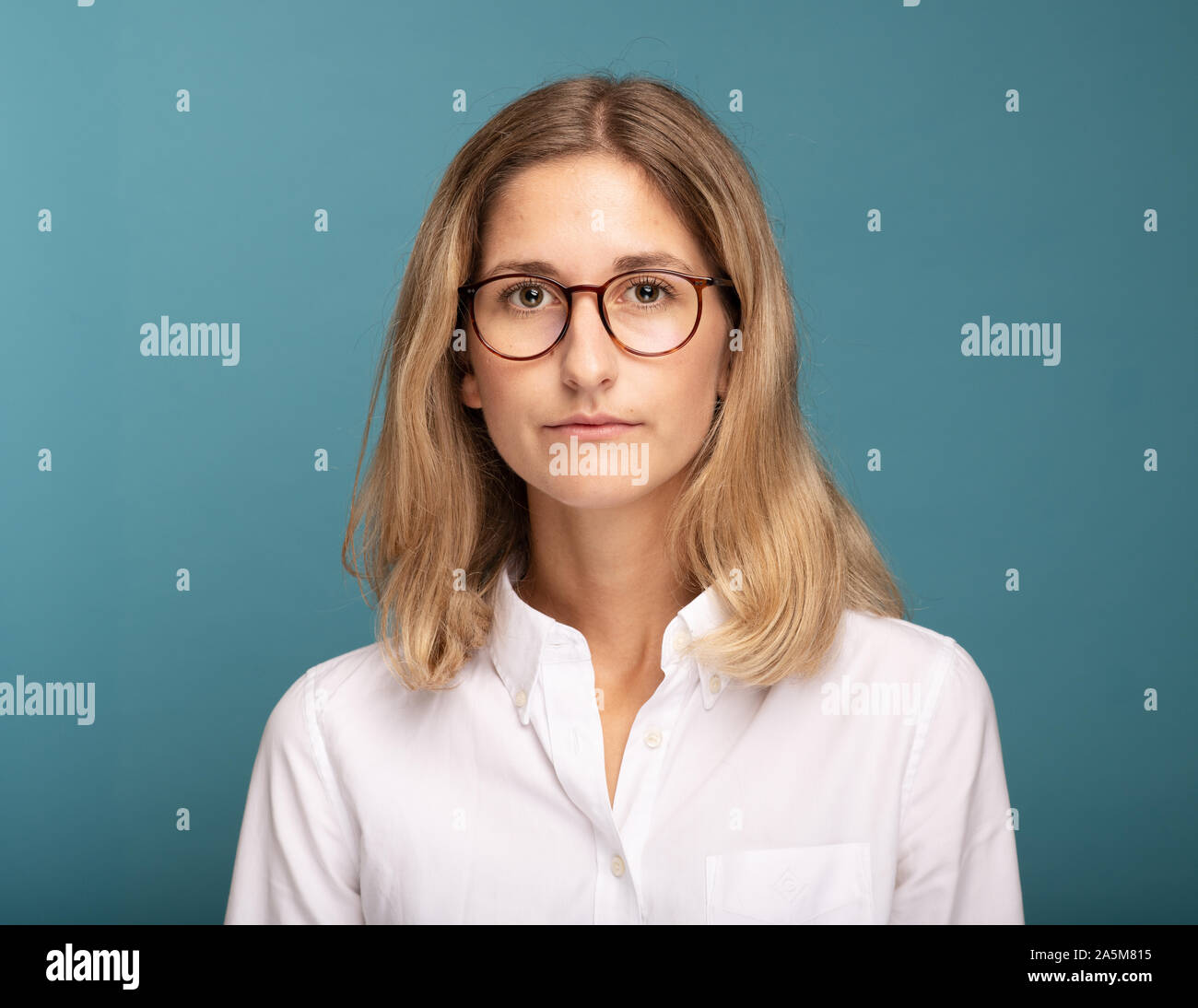 Ritratto di una bionda imprenditrice con gli occhiali di fronte a sfondo blu Foto Stock