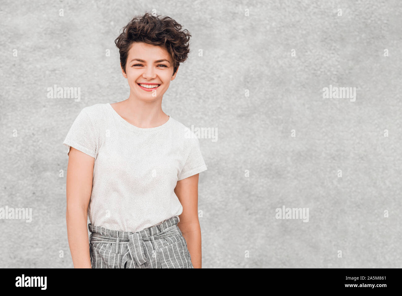 Affascinante giovane donna con acconciatura di creative è sempre sorridente e in posa con gioiosa faccia felice. Emozioni e sentimenti. Foto Stock