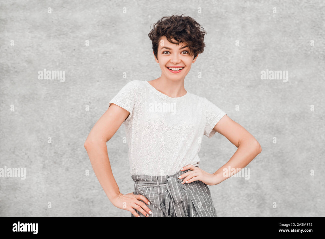 Affascinante giovane donna con acconciatura di creative è sempre sorridente e in posa con gioiosa sorpresi di fronte. Emozioni e sentimenti. Foto Stock