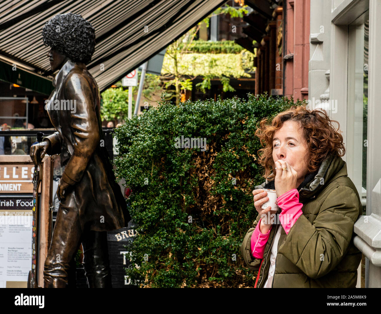 Donna di fumare accanto alla statua di Luca Kelly, St Stephen's area verde, Dublino, IRLANDA REGNO UNITO Foto Stock