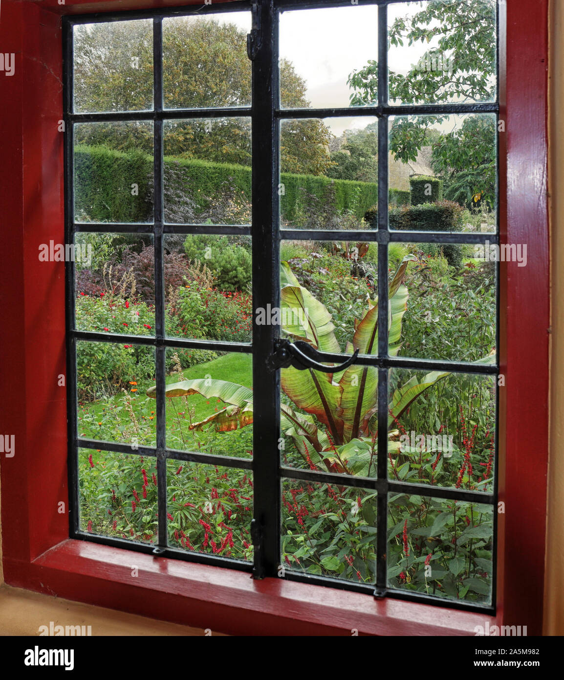Un inglese formale giardino paesaggistico con percorso erboso visto attraverso una finestra Foto Stock