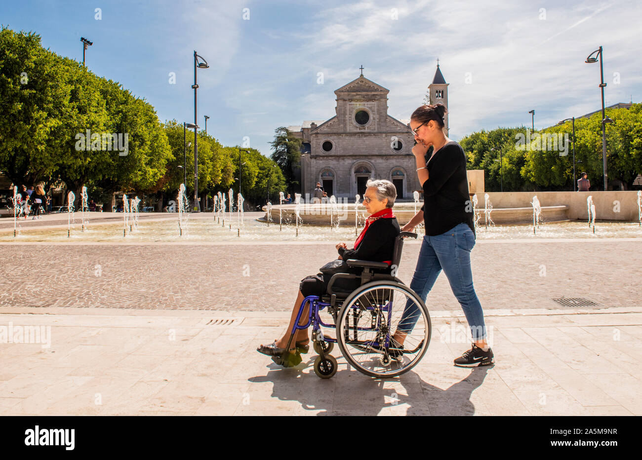 Donna madre di spinta sulla sedia a rotelle, Piazza Risorgimento, Avezzano, Abruzzo, Italia Foto Stock