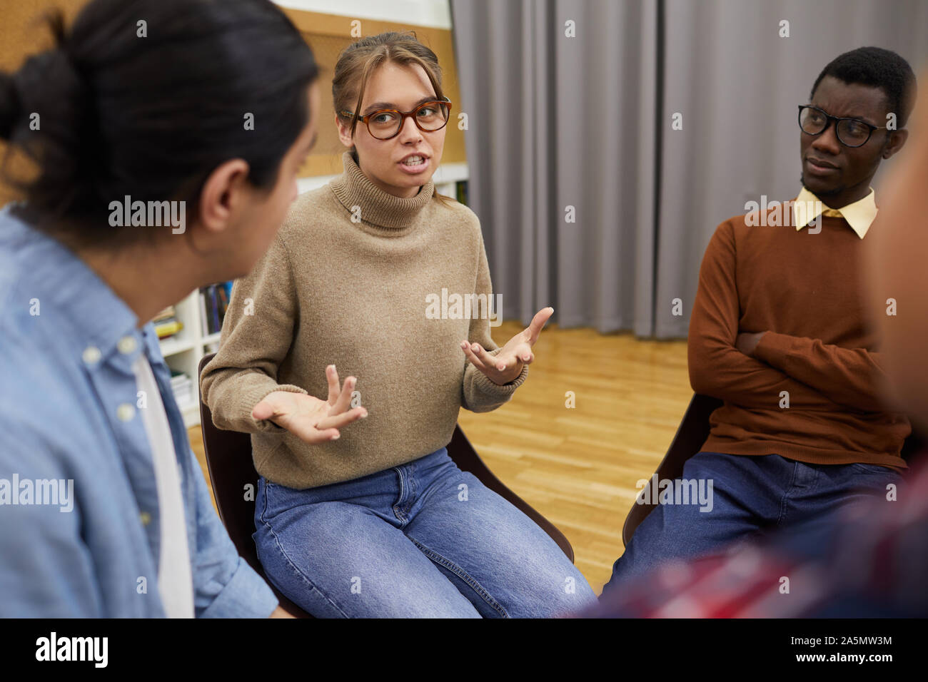 Ritratto di giovane donna gesticolando attivamente durante la partecipazione nel gruppo di assistenza discussione, spazio di copia Foto Stock