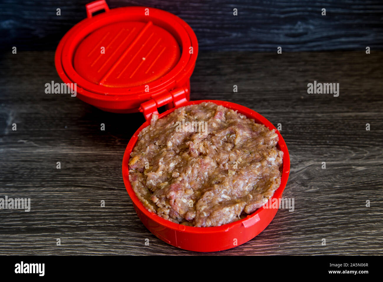 In plastica rosso burger imbottitore. Carne di manzo e di maiale polpette di carne macinata essendo ripieni con pancetta croccante, grossi pezzi di formaggio Colby. Mostra premere in uso con prodotti crudi Foto Stock