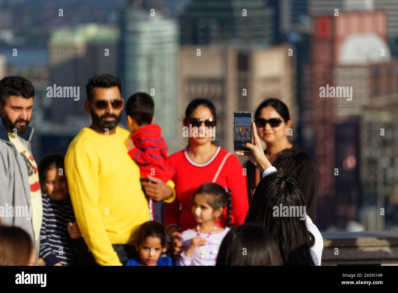 A n asian lady di scattare una foto della sua famiglia sul belvedere Kondiaronk su Montreals Mont Royal, con i grattacieli del centro cittadino di oltre Foto Stock