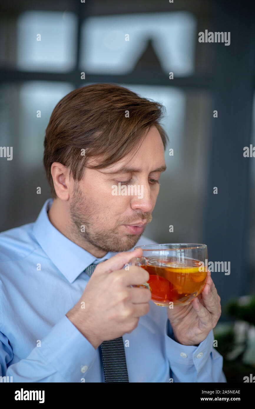 Dai capelli scuri lavoratore di ufficio soffiando a il suo tè Foto Stock