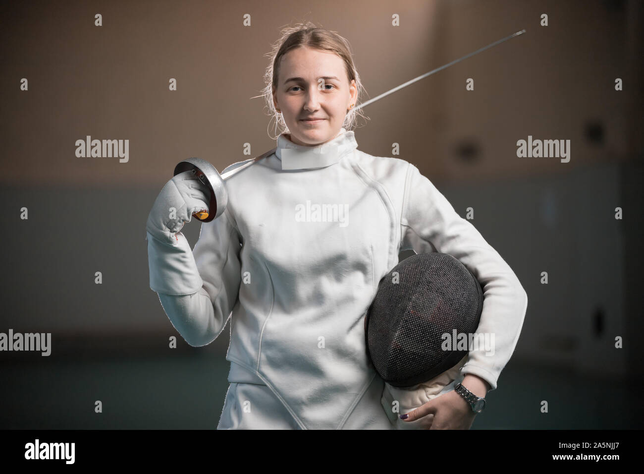 Donna sorridente fencer in piedi nella palestra della scuola con la spada dietro la schiena. Metà shot Foto Stock
