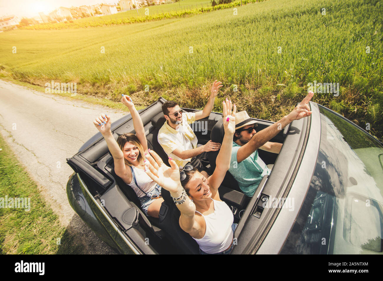 Gruppo di amici divertendosi al viaggio in auto. Quattro persone caucasica su una vettura sportiva con in alto le mani. Foto Stock