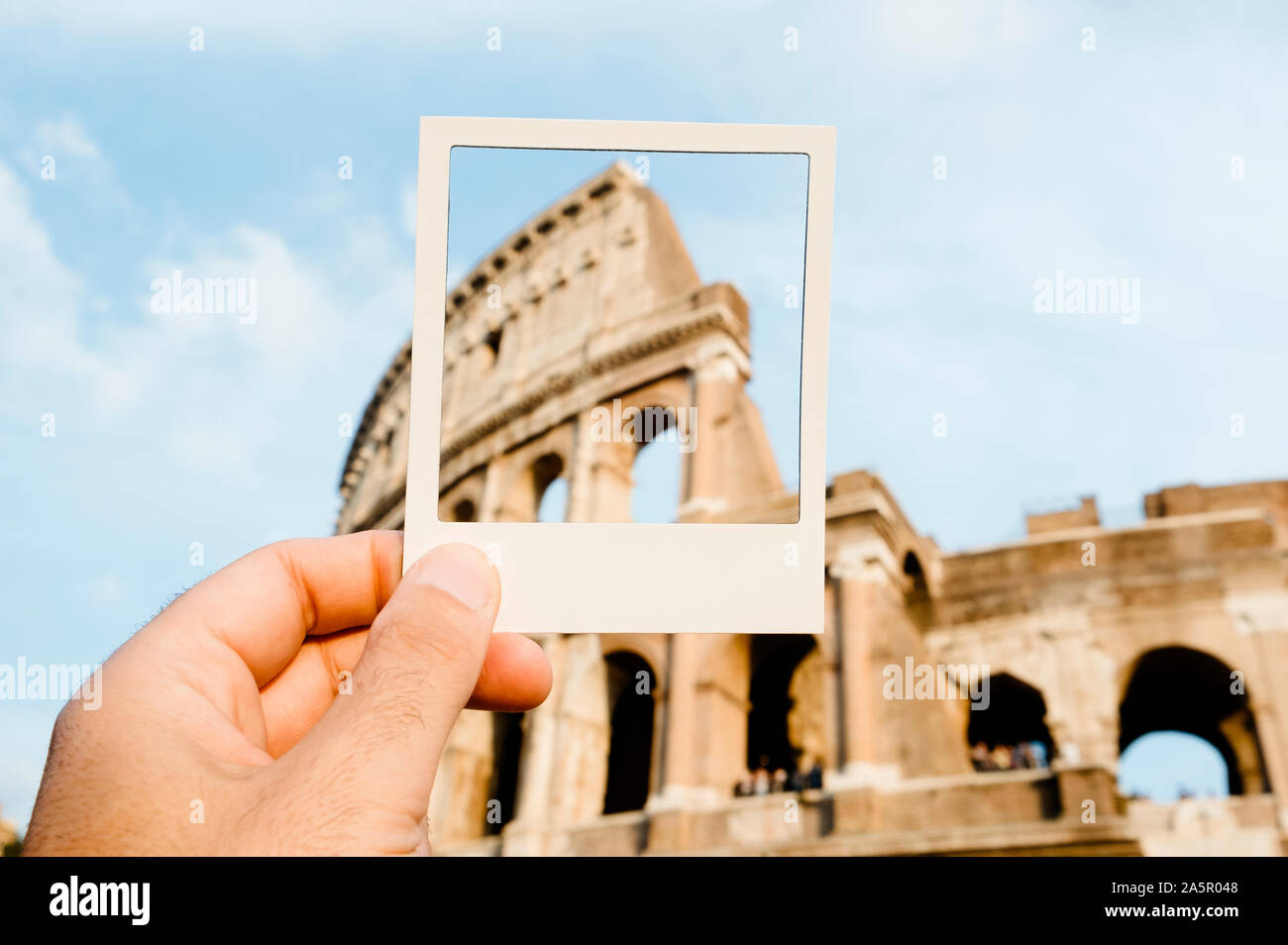 Primo piano di un giovane uomo con una cornice bianca in mano, inquadrando il famoso Anfiteatro Flavio o Colosseo a Roma, in Italia, simulando un istante pho Foto Stock