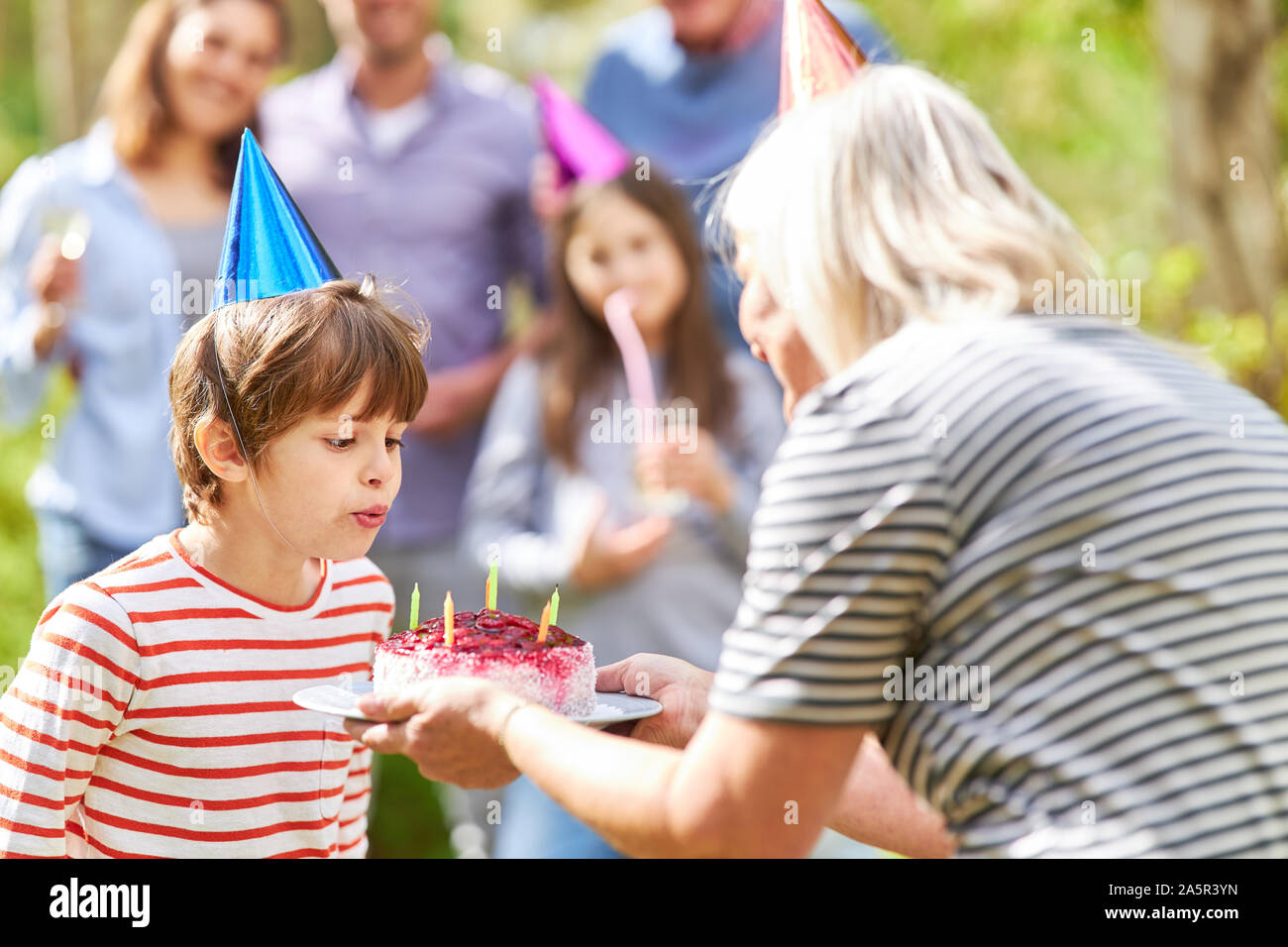 Il ragazzo si brucia le candele sulla sua torta di compleanno in giardino in estate Foto Stock
