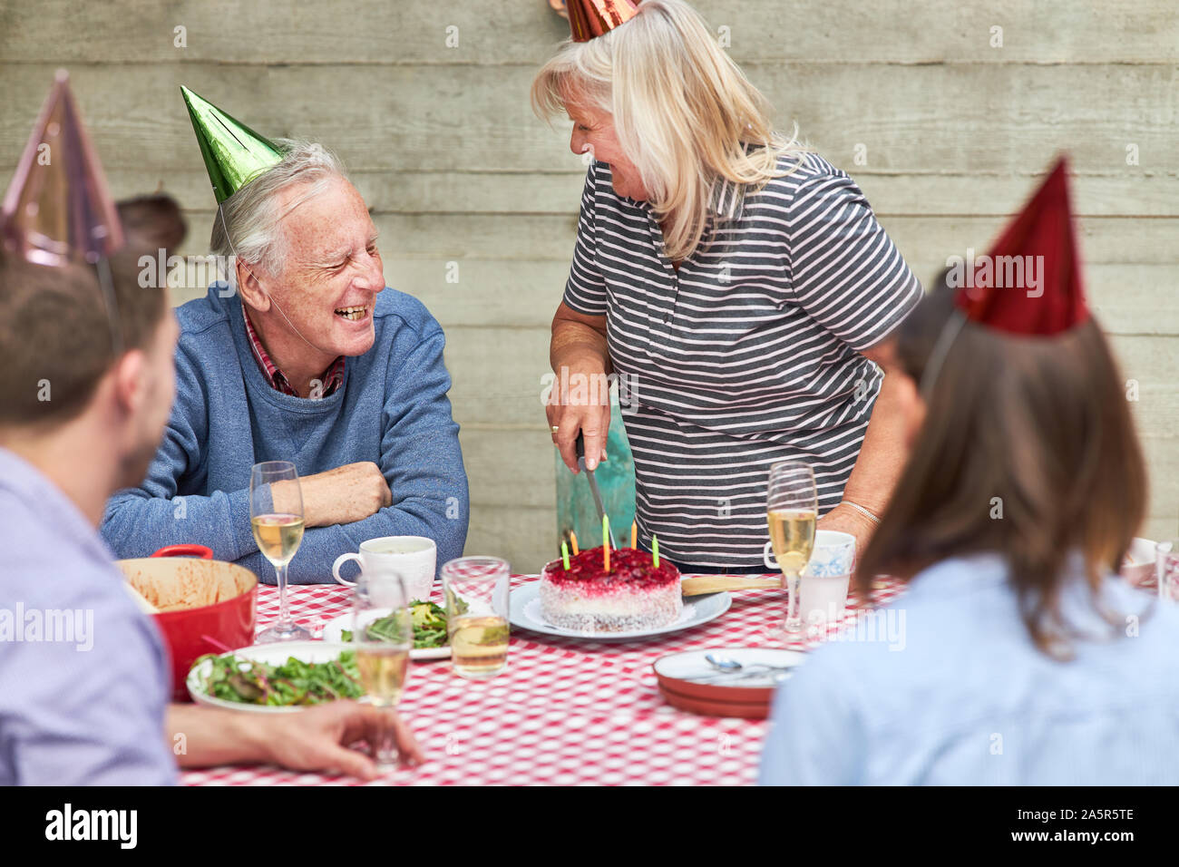 Seniors celebrare con la loro famiglia compleanno con torta nel giardino in estate Foto Stock