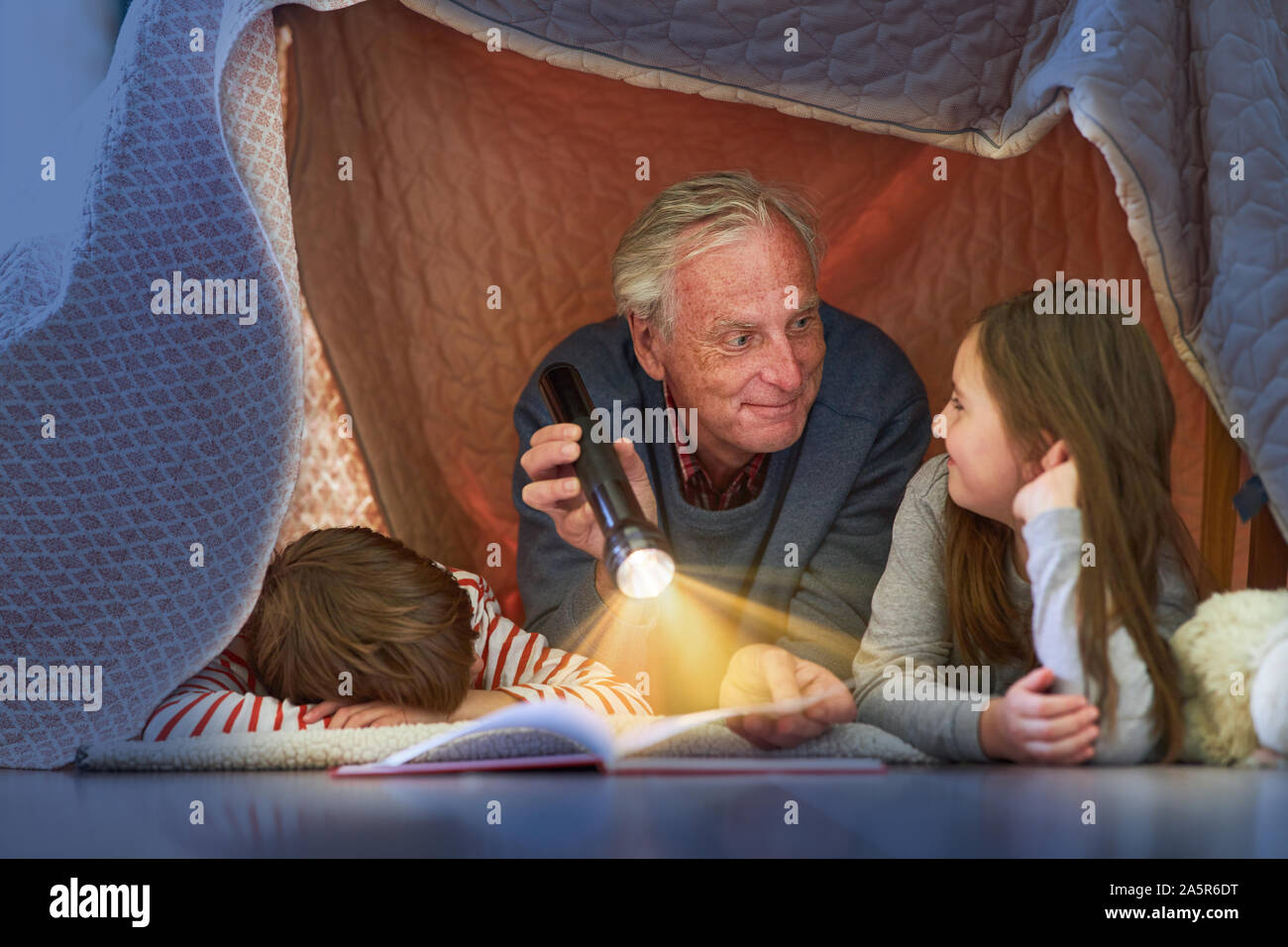 Il nonno legge nipoti storia sotto una coperta come una tenda a casa Foto Stock